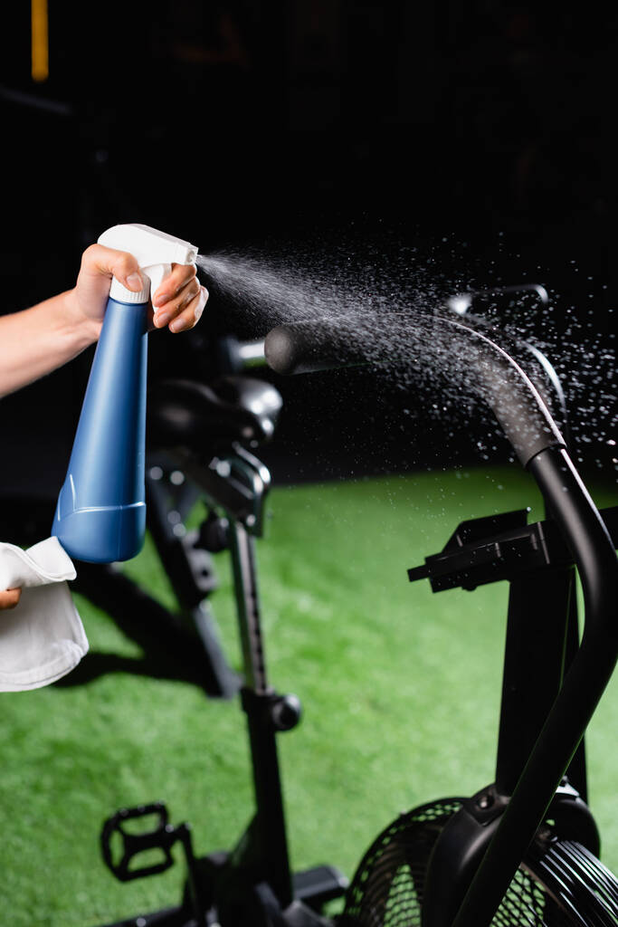 vista parziale di charwoman spruzzando detergente su attrezzature sportive in palestra - Foto, immagini