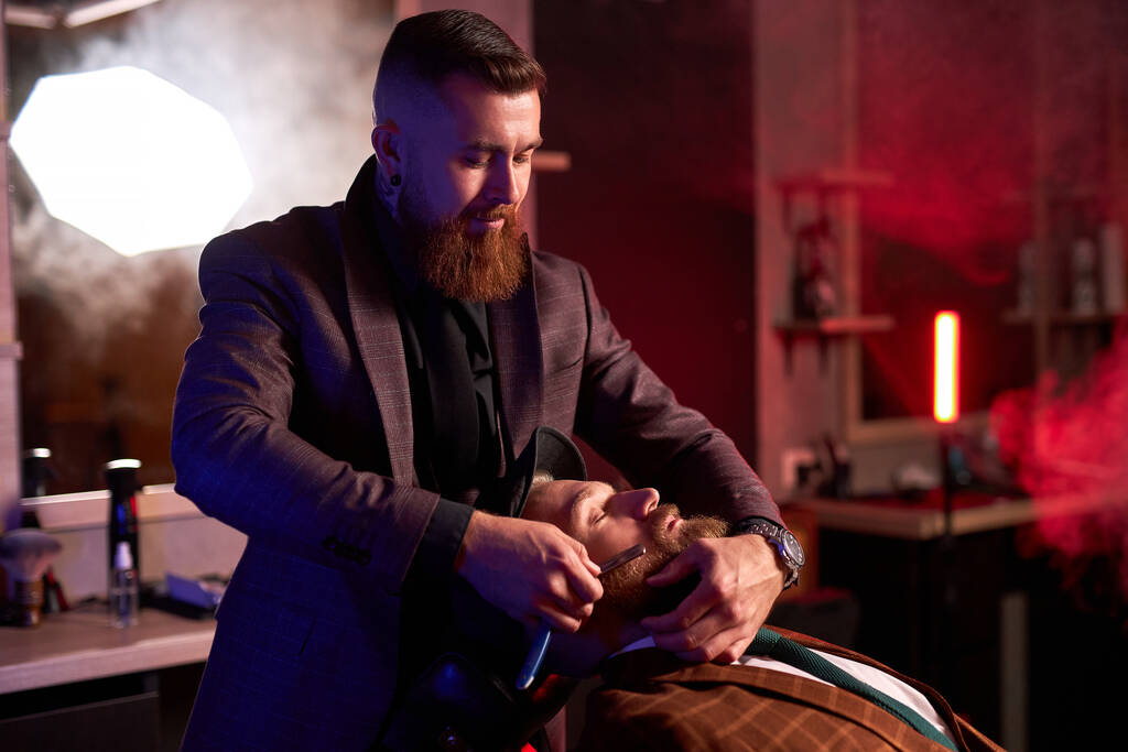 biały hipster klient człowiek odwiedzając w fryzjer sklep golenie broda przez profesjonalny fryzjer - Zdjęcie, obraz