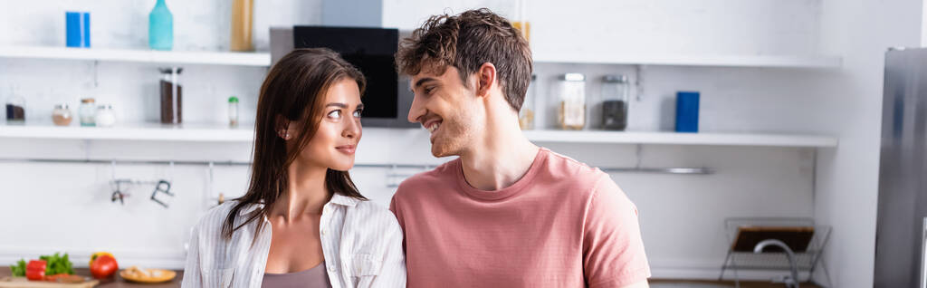 Hombre sonriente mirando a su novia en la cocina, pancarta - Foto, imagen