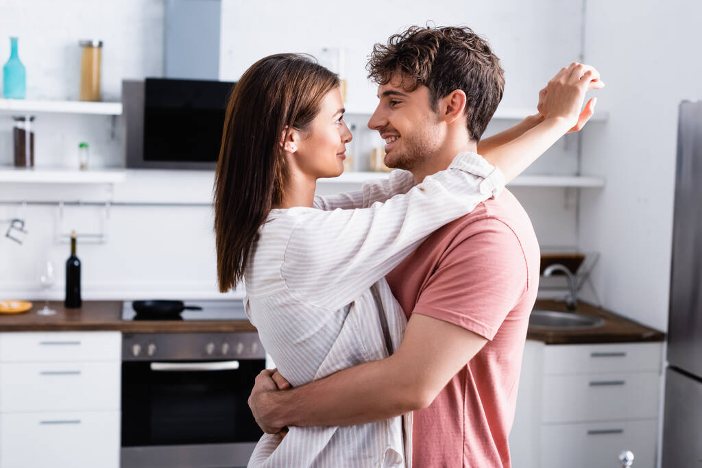 Usmívající se muž objímající přítelkyni v kuchyni doma  - Fotografie, Obrázek