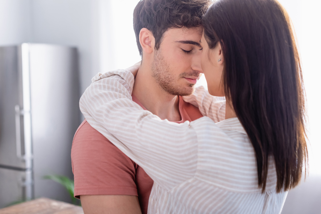 Brunette woman hugging boyfriend with closed eyes at home  - Photo, Image
