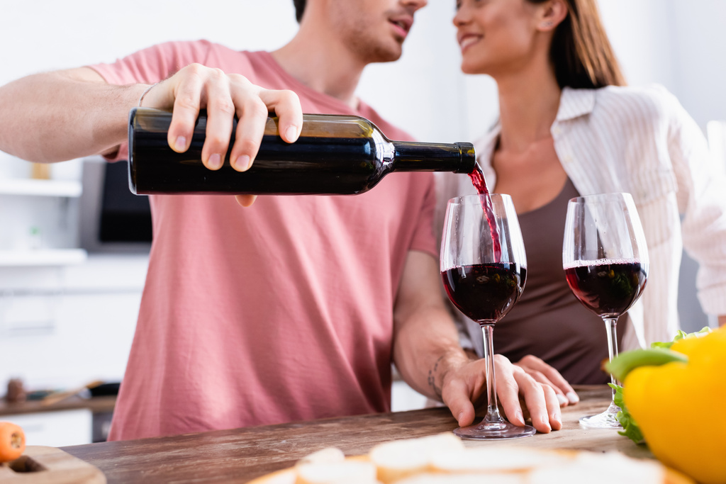 Обрезанный вид человека, наливающего вино в бокал рядом с девушкой на размытом переднем плане  - Фото, изображение