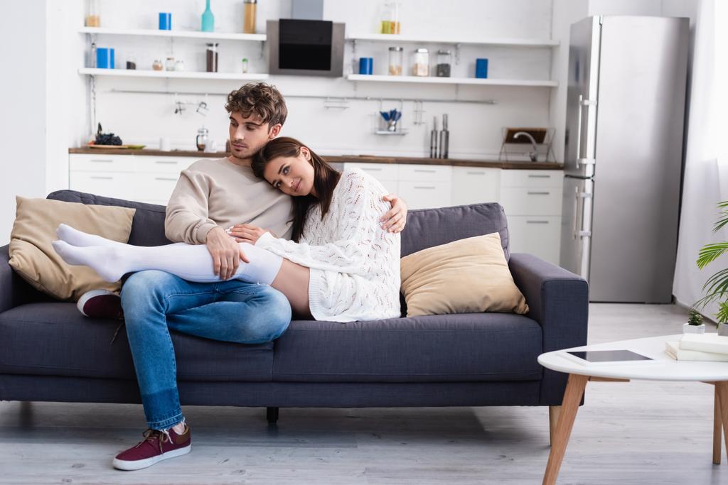 Sorridente donna in ginocchio calze abbracciare fidanzato sul divano  - Foto, immagini