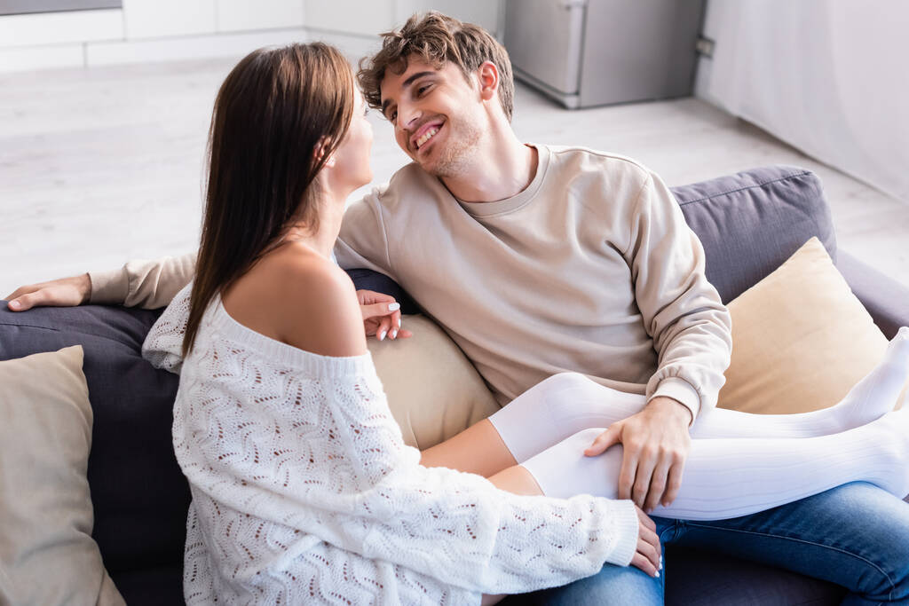 Smiling man touching legs of girlfriend in knee socks on couch  - Photo, Image