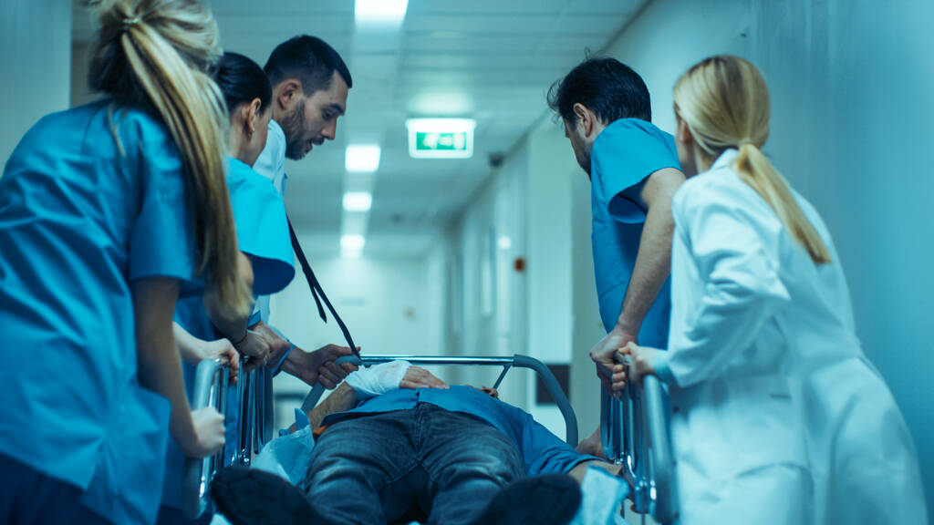 Emergency Department: Doctors, Nurses and Surgeons Move Seriously Injured Patient Lying on a Stretcher Through Hospital Corridors. Medical Staff in a Hurry Move Patient into Operating Theater. - Photo, Image
