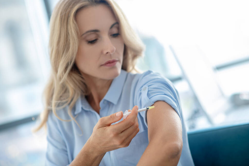 Szőke nő adja be az injekciót a karjába - Fotó, kép