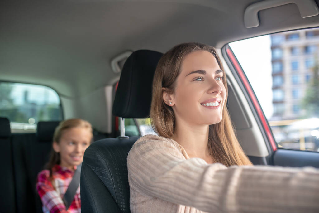 Χαμογελώντας μαμά οδήγηση με την κόρη της κάθεται στο πίσω κάθισμα του αυτοκινήτου - Φωτογραφία, εικόνα