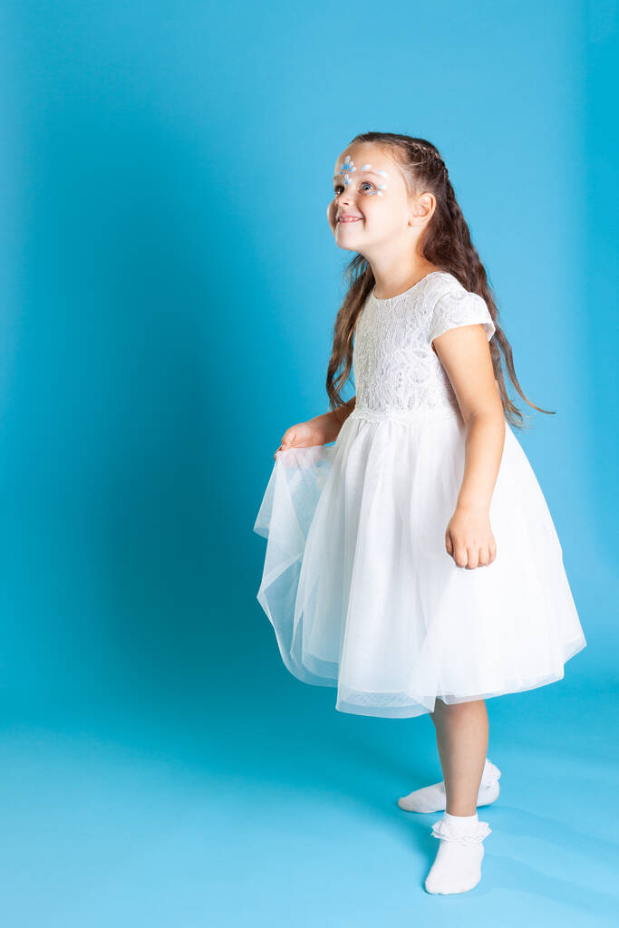 pełnowymiarowy portret dziewczyny w białej sukience księżniczki stojącej bokiem i patrzącej z uśmiechem odizolowanym na niebieskim tle, przestrzeń kopiowania - Zdjęcie, obraz