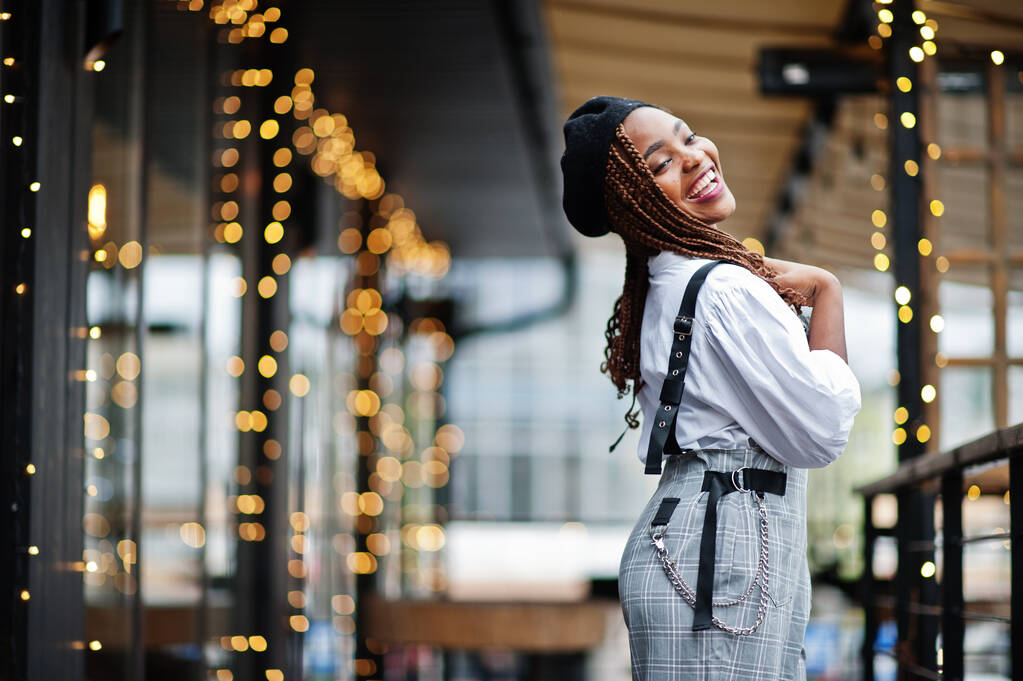African american woman in overalls and beret posed in outdoor terrace with christmas decorations garland. - Photo, Image