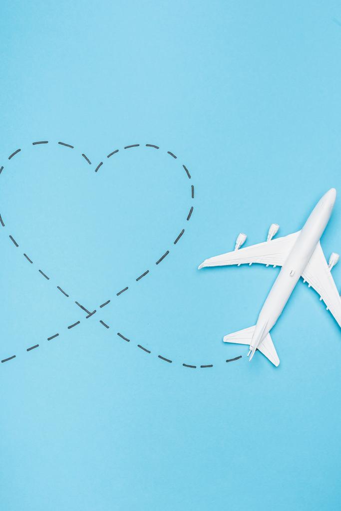 Draufsicht auf weißes Flugzeugmodell und Herz auf blauem Hintergrund - Foto, Bild
