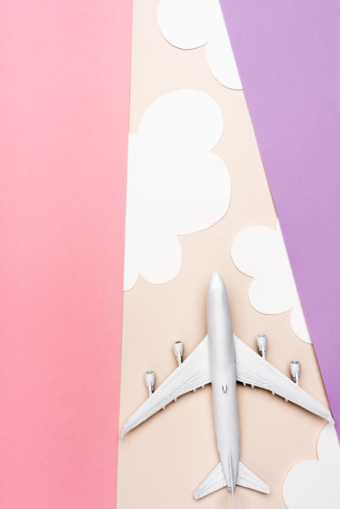 Draufsicht des weißen Flugzeugmodells auf buntem Hintergrund mit Wolken - Foto, Bild
