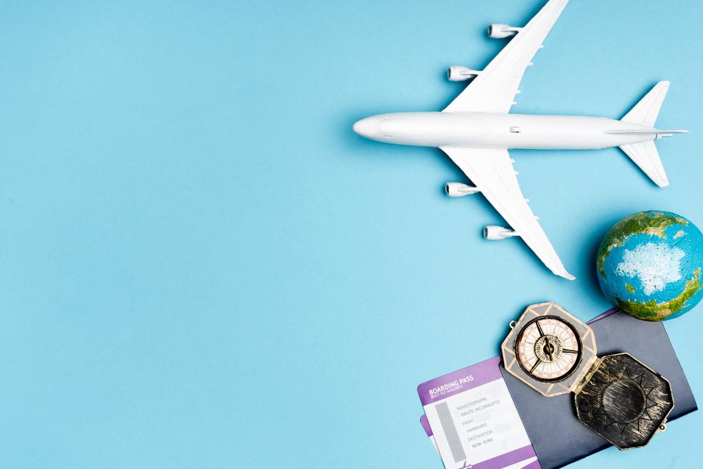 Draufsicht auf weißes Flugzeugmodell, Kompass, Globus und Tickets auf blauem Hintergrund - Foto, Bild