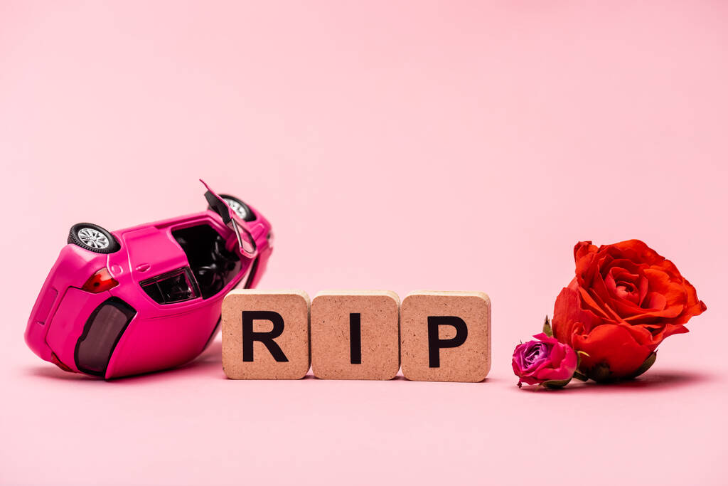 összetört autó és szó rip virágokkal rózsaszín háttér - Fotó, kép
