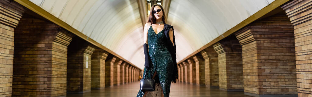 модна жінка в довгій чорній сукні і сонцезахисних окулярах позує на підземній станції, банер
 - Фото, зображення