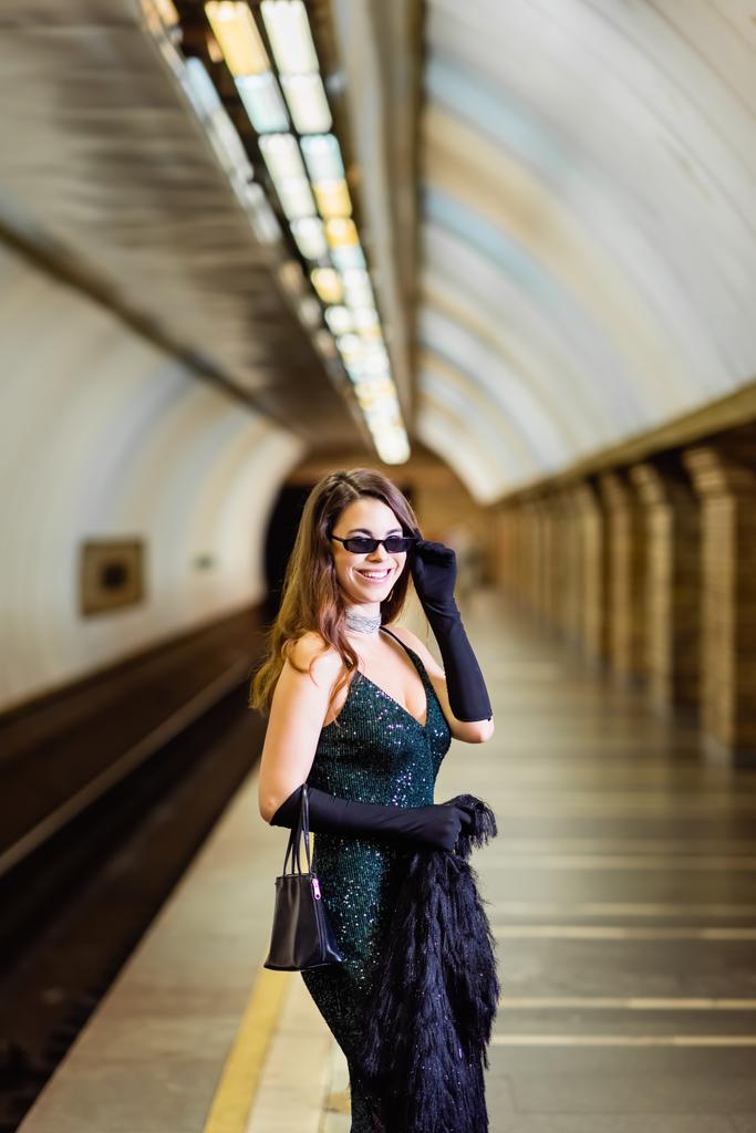 elegáns nő fekete lurex ruha mosolyog a kamera metró állomás platform - Fotó, kép