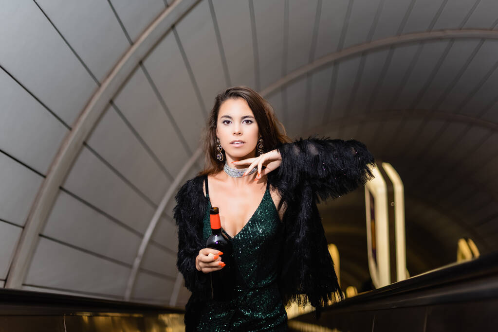 cropped view of glamour woman posing on escalator with bottle of wine - Photo, Image