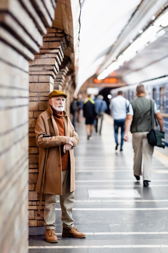w wieku mężczyzna jesienią strój stojący w pobliżu ludzi i trenować na peronie metra na zamazanym pierwszym planie - Zdjęcie, obraz