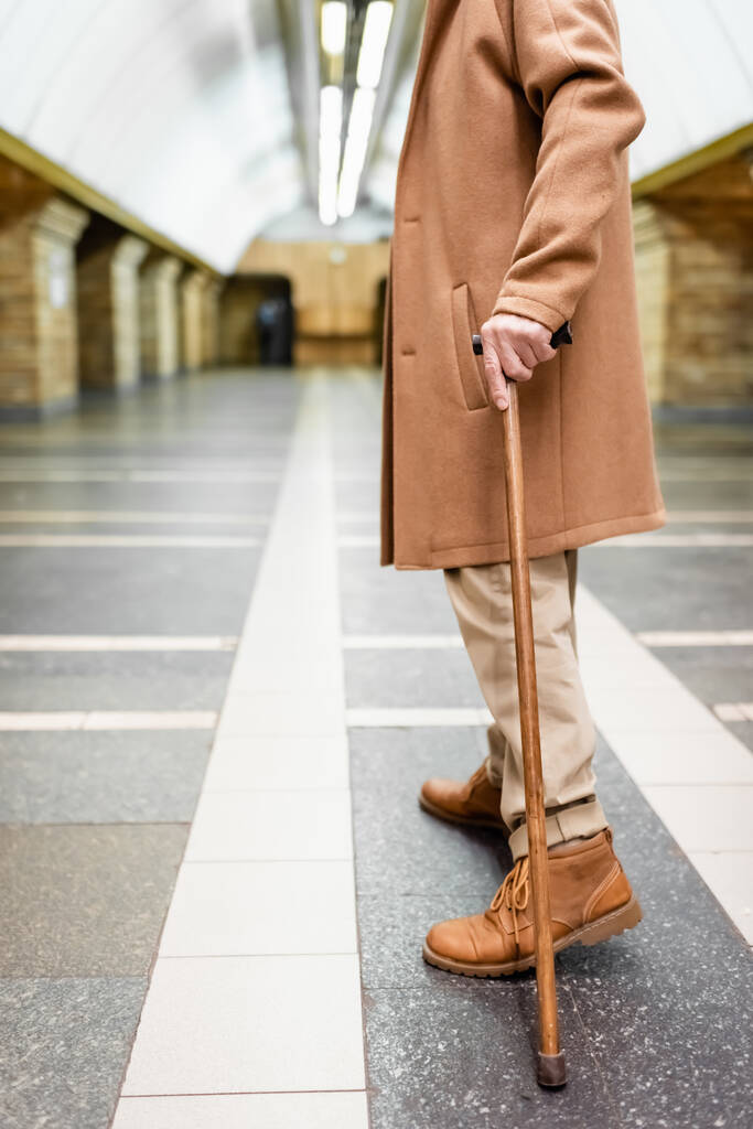 歩行棒を持つ男のクロップドビュー秋の衣装で地下鉄駅に立って - 写真・画像