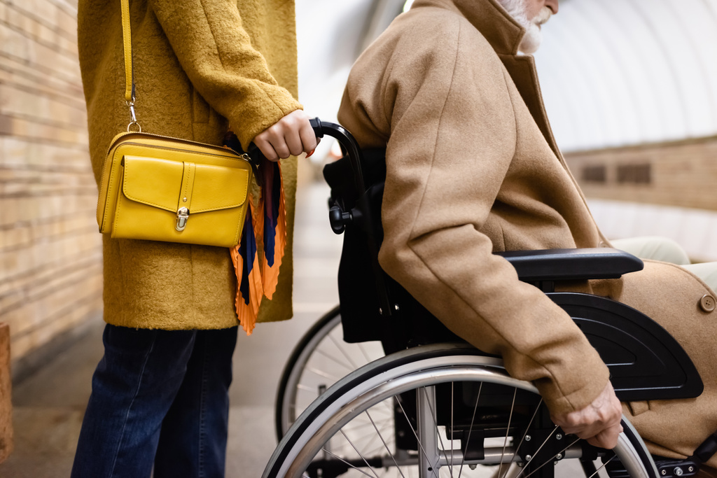 levágott kilátás nő gazdaság kerekesszék idős fogyatékkal élő férfi metró állomáson - Fotó, kép