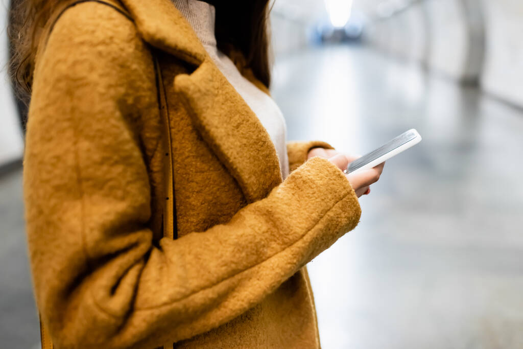 partial view of woman in coat messaging on mobile phone on blurred foreground - Foto, imagen
