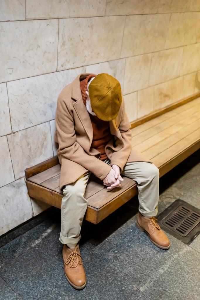 idős férfi őszi kabát és sapka alszik underground platform padon - Fotó, kép