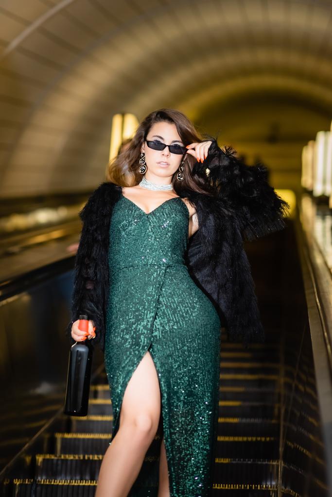 vue recadrée de glamour femme posant sur escalator avec bouteille de vin - Photo, image