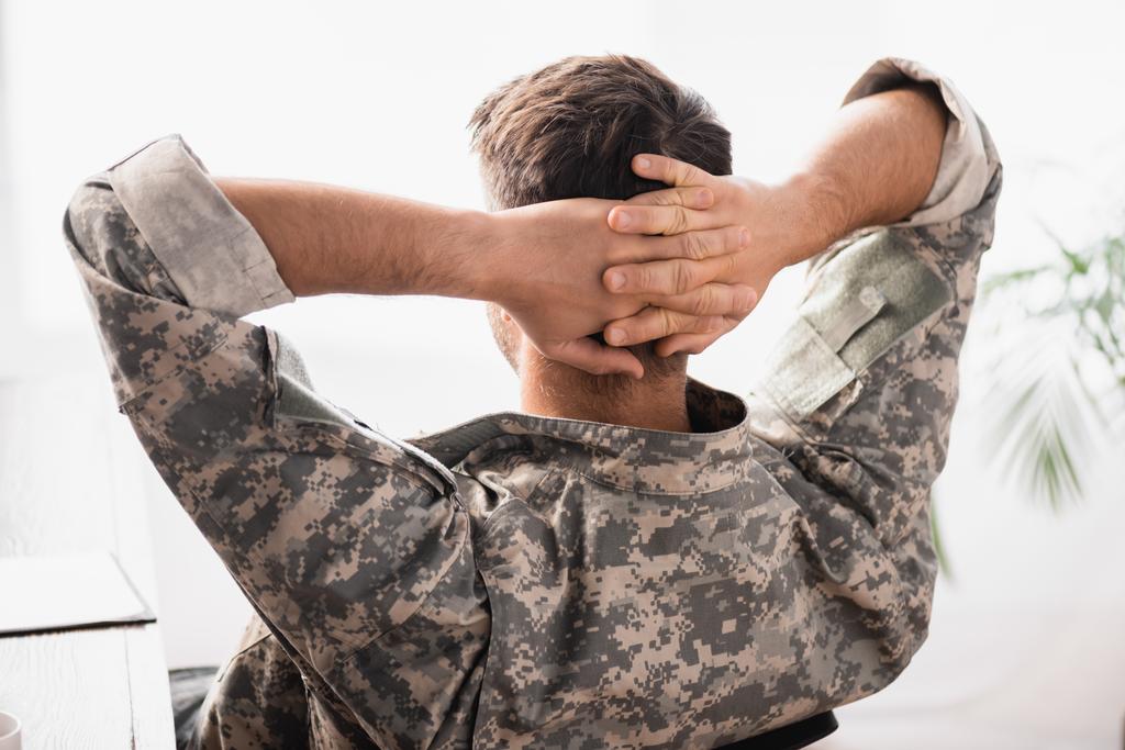 πίσω όψη στρατιώτη με στρατιωτική στολή με τα χέρια πίσω από την πλάτη να αναπαύονται στο γραφείο - Φωτογραφία, εικόνα