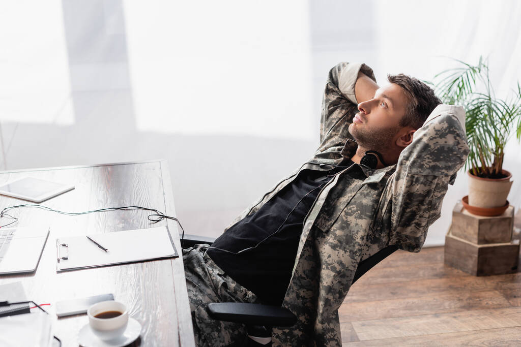 軍の制服を着た兵士と椅子のガジェットの近くに眠るヘッドセット - 写真・画像