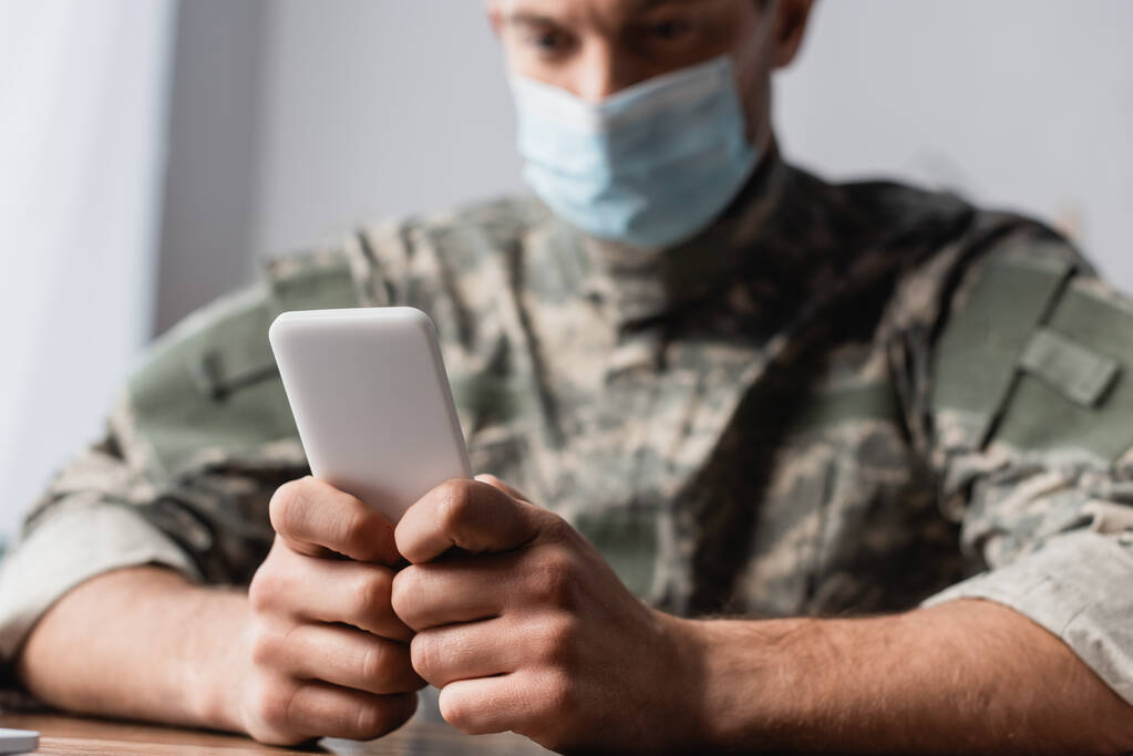 smartfon w rękach na żołnierza w mundurze i maska medyczna na rozmytym tle - Zdjęcie, obraz