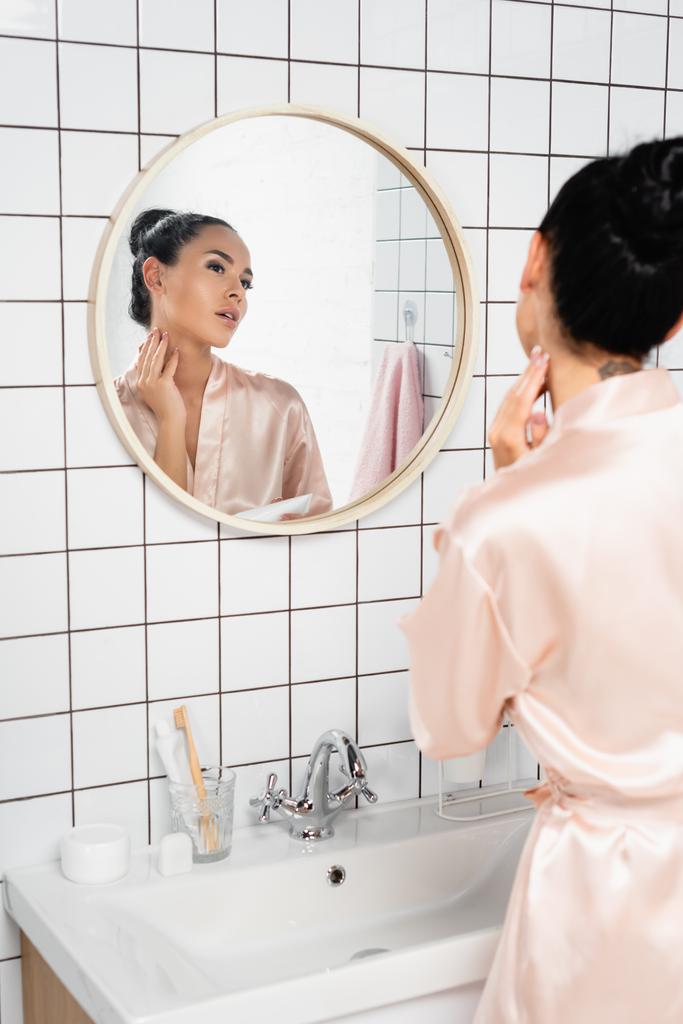 Жінка з Брюнета наносить косметичне крем біля раковини і дзеркала у ванній кімнаті.  - Фото, зображення