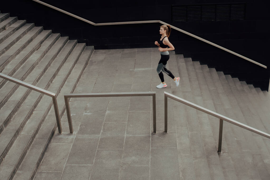 Uma jovem de fato de treino sobe as escadas, num centro de negócios. - Foto, Imagem