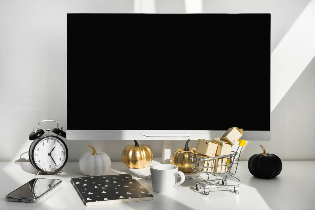 Pusty ekran komputera biurkowego w nowoczesnym minimalnym pomieszczeniu biurowym z dekoracjami jesiennymi. Papierowe pudełka w wózku na biurku. Koncepcja zakupów online - Zdjęcie, obraz