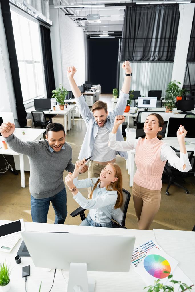 Веселі багатокультурні бізнесмени показують так жест біля комп'ютера і барвисті годинники на офісному столі
  - Фото, зображення