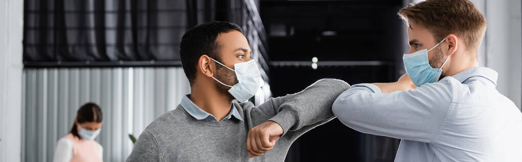 Мультиэтнические бизнесмены в медицинских масках дают пять с локтями в офисе, баннер  - Фото, изображение