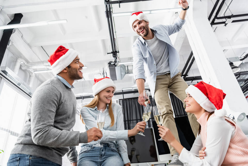 オフィスでクリスマスを祝うシャンパンとサンタの帽子の眼鏡を持つ多民族のビジネスマン  - 写真・画像