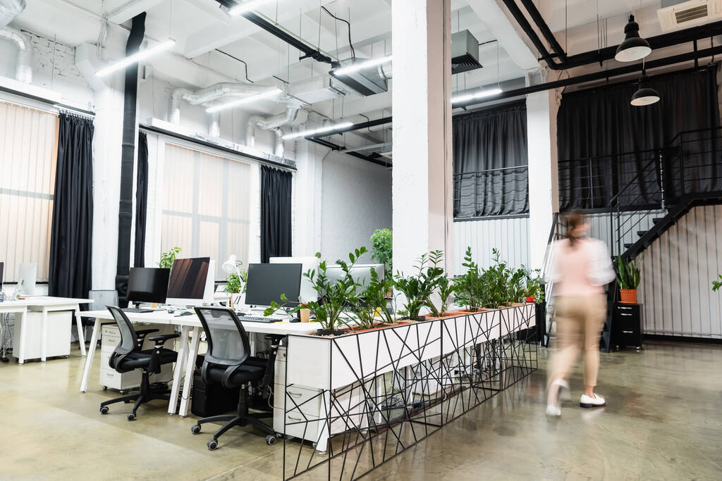 Rozmazání pohybu podnikatelky kráčející v blízkosti počítačů a rostlin v kanceláři  - Fotografie, Obrázek