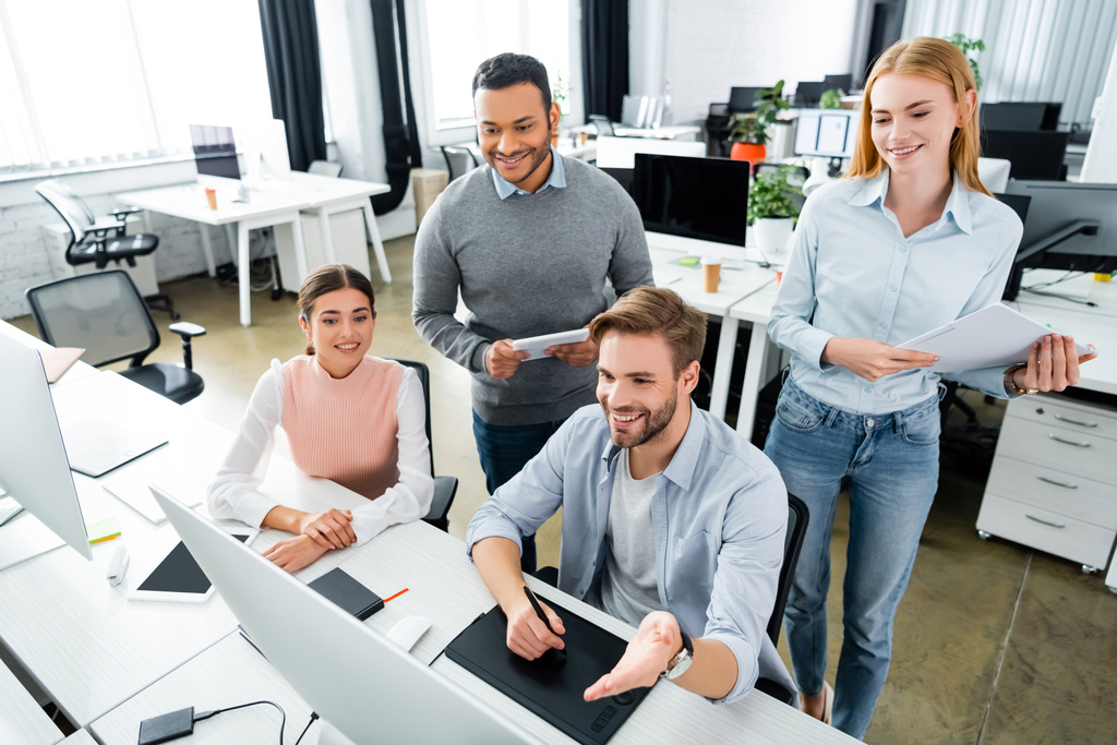 Lächelnde multikulturelle Geschäftsleute mit Grafik-Tablet und Computer im Büro  - Foto, Bild