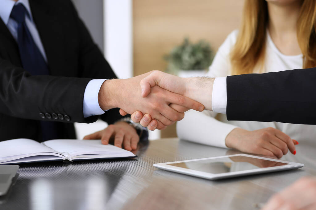 Businessman shaking hands with his colleague or partner above the glass desk in modern office, close-up. Unknown business people at meeting. Teamwork, partnership and handshake concept - Photo, Image