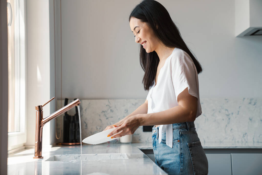 Immagine di una giovane allegra ottimista a casa a lavare i piatti - Foto, immagini