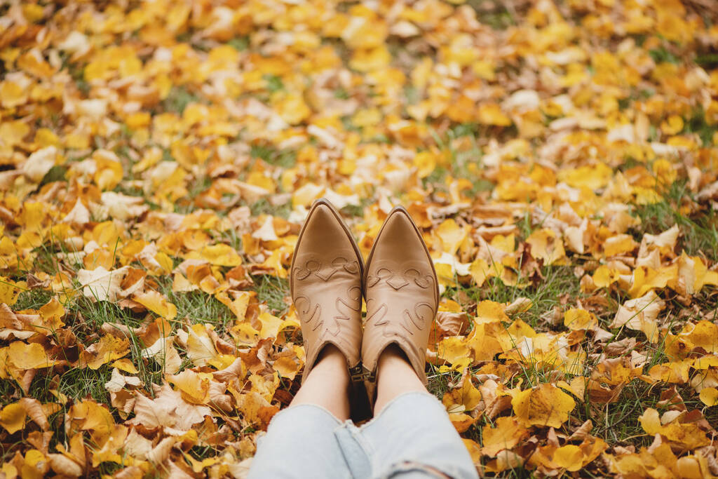 Patas de mujer en botas de vaquero en las hojas de otoño. - Foto, imagen