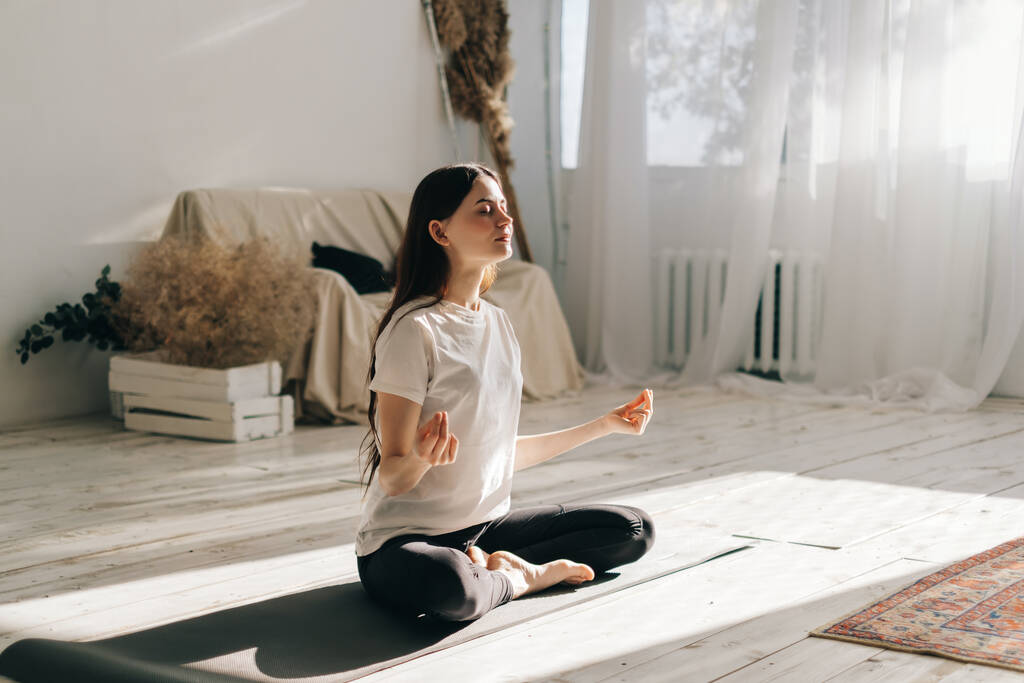 Mooie brunette fitness vrouw mediteren, doen yoga binnen thuis. Gezond en fit blijven - Foto, afbeelding