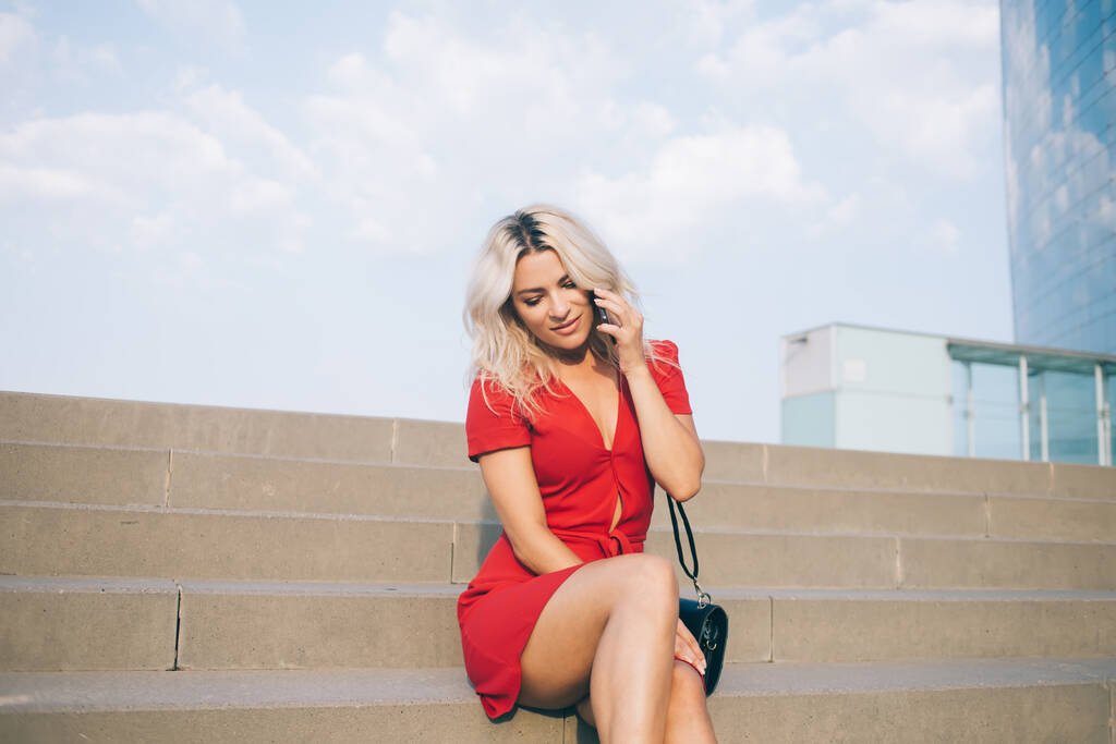 Καλαίσθητο hipster κορίτσι απολαμβάνοντας κυτταρική συνομιλία κατά τη διάρκεια του χρόνου ανάπαυσης στην urbanity, όμορφη γυναίκα σε κομψό κόκκινο sundress λαμβάνουν φιλική κλήση για συζήτηση σόλο ταξίδια μέσω smartphone gadget - Φωτογραφία, εικόνα