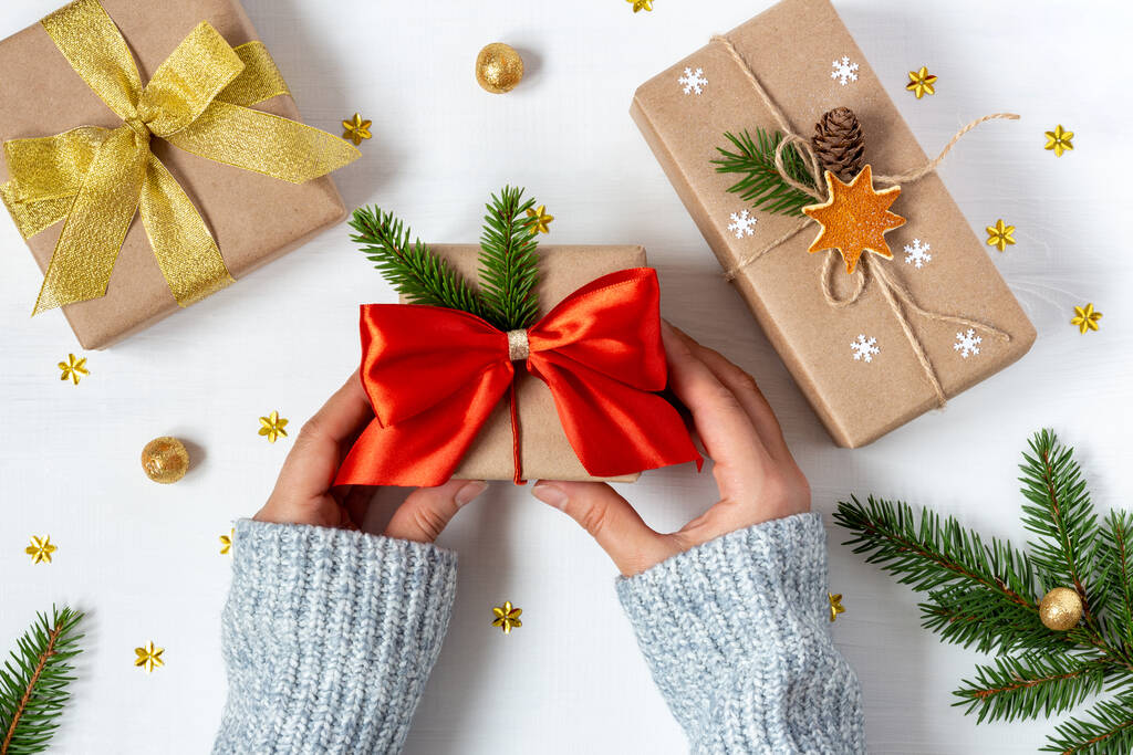 ウールのセーターの女性の手は、エコペーパーで2つのプレゼントの横にヴィンテージスタイルで包まれた贈り物を保持します - 写真・画像