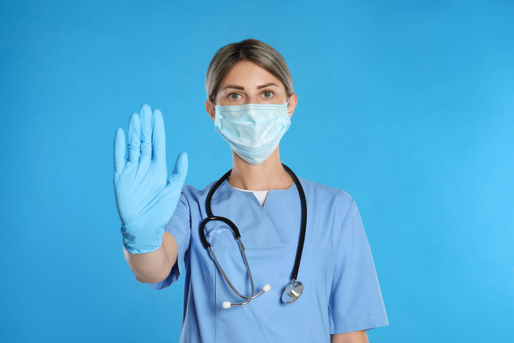 Доктор у захисній масці, що показує стоп- жест на світло-блакитному тлі. Запобігання поширенню коронавірусу
 - Фото, зображення