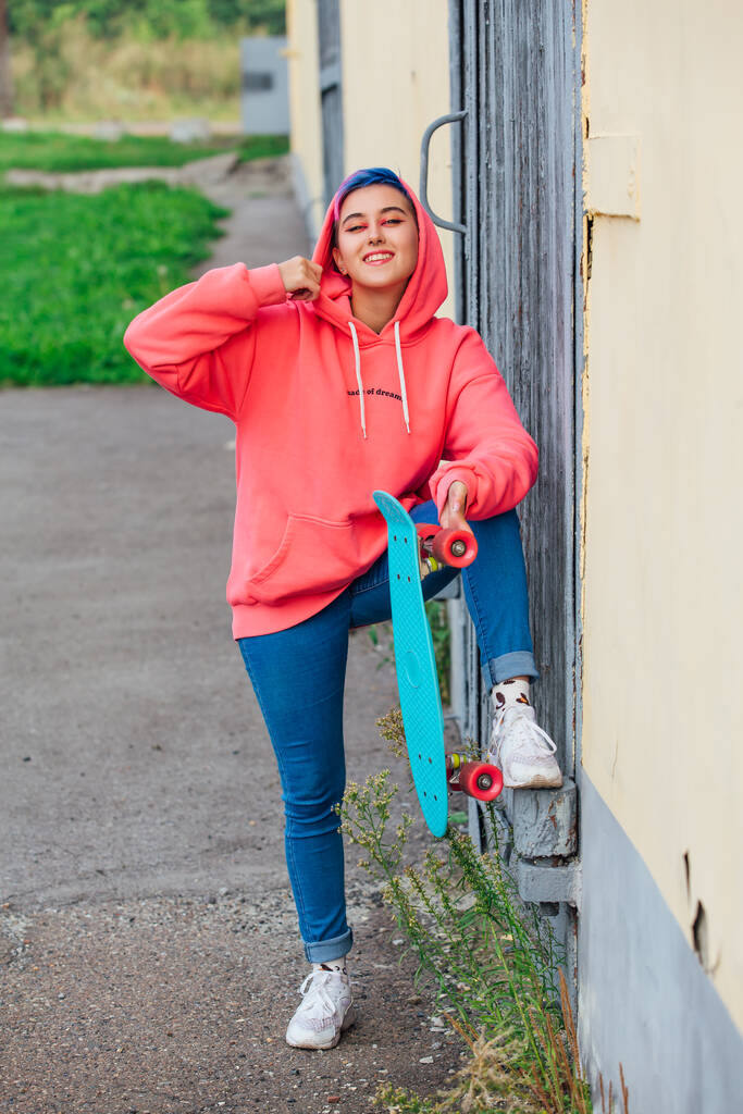 Elegante giovane donna con i capelli corti colorati tenendo in mano lo skateboard di plastica blu. Concetto gioventù. - Foto, immagini