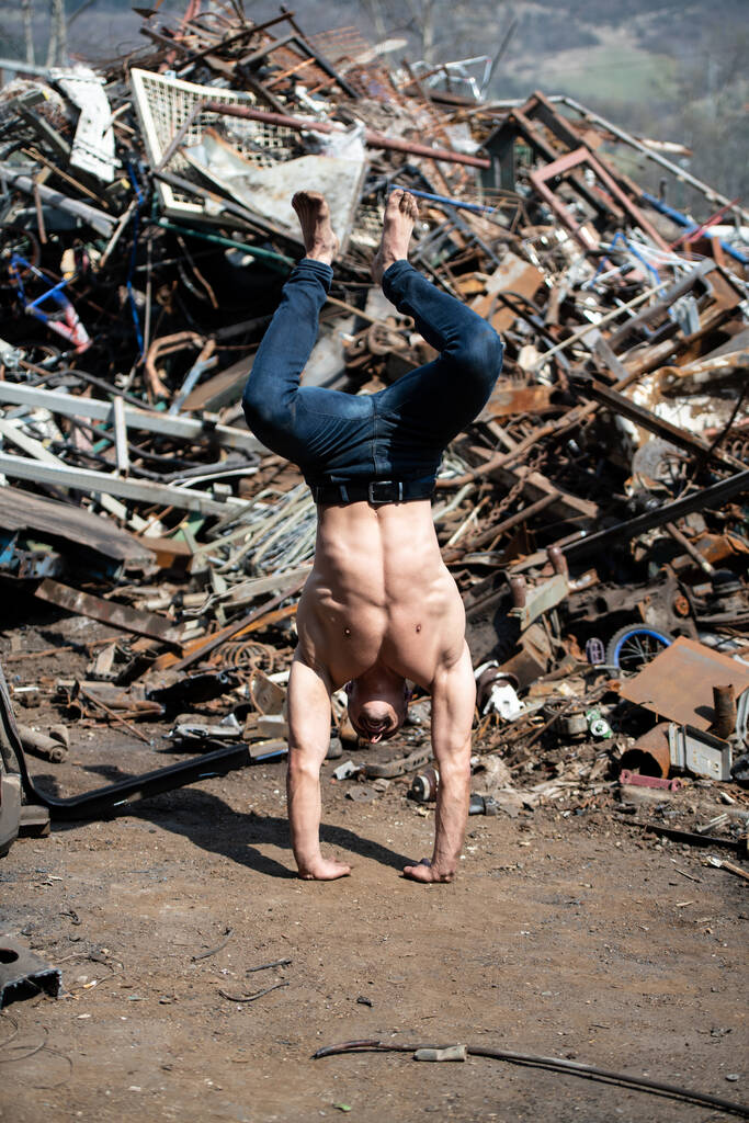 Młody człowiek utrzymujący równowagę na rękach w starym przemysłowym złomowisku - Muscular Athletic Bodybuilder Fitness Model Doing Handstand push-up - Zdjęcie, obraz