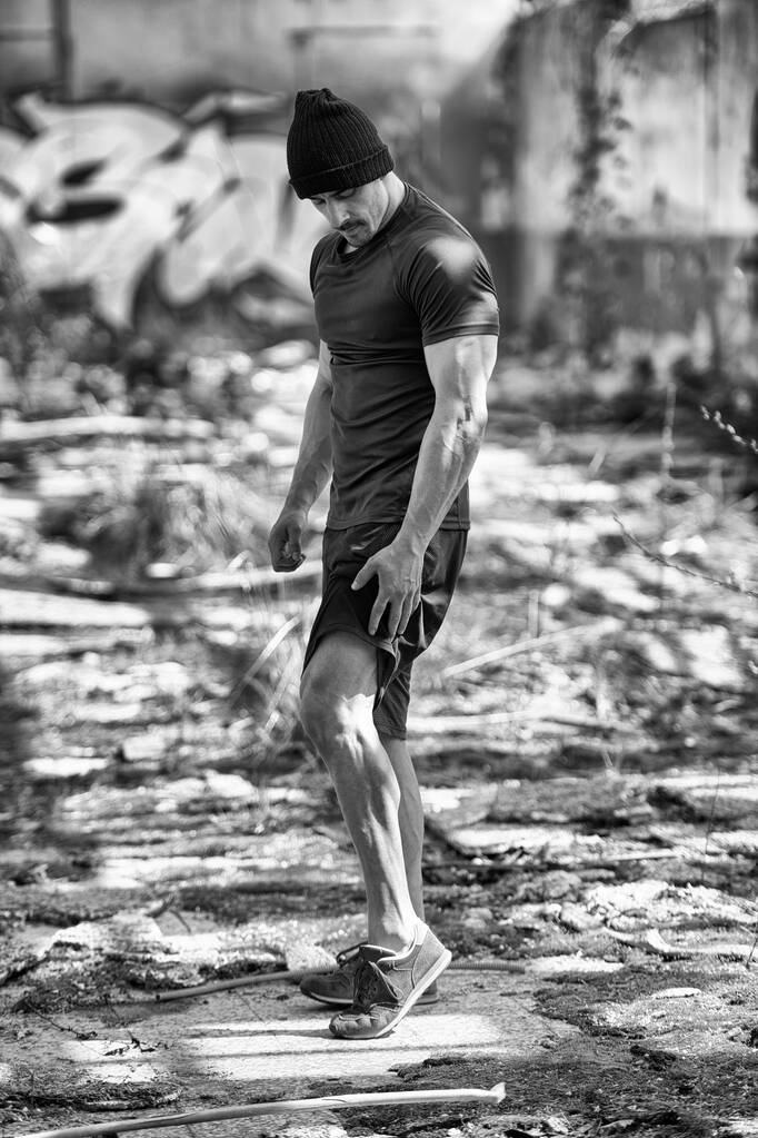 Porträt eines jungen, körperlich fitten Mannes, der in einer Lagerhalle steht und seinen gut trainierten Körper zeigt - Foto, Bild