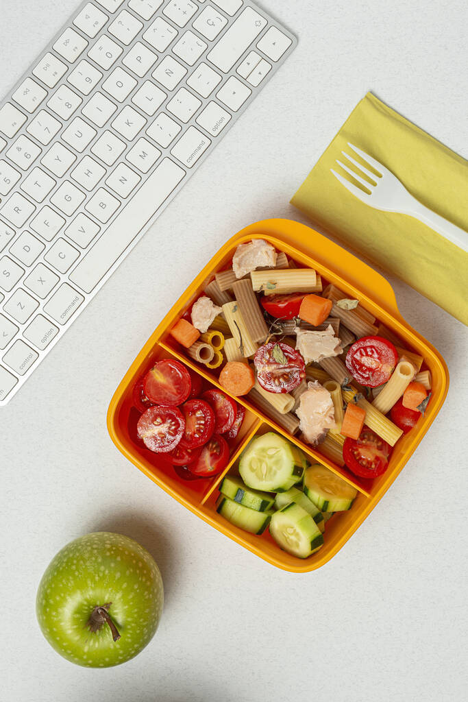 Lunch at work place healthy pasta with tuna, cherry tomatoes, carrot, cucumber in lunch box on work table. Home food for office concept - Photo, Image