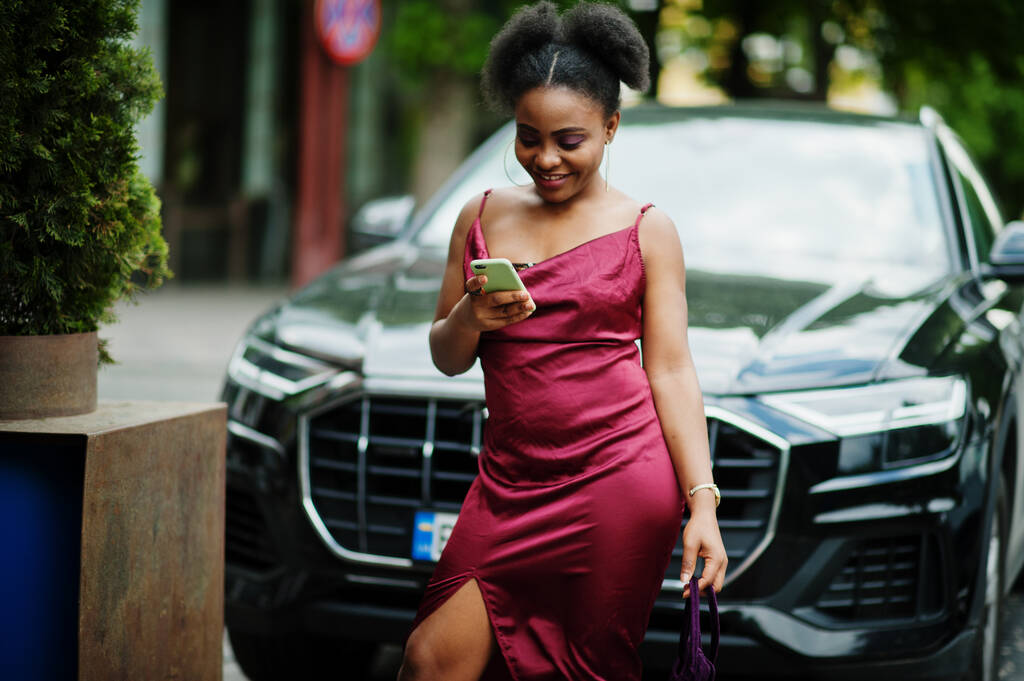 Porträt einer schönen natürlichen jungen Afrikanerin mit Afrohaaren. Schwarzes Model im roten Seidenkleid mit Handy. - Foto, Bild