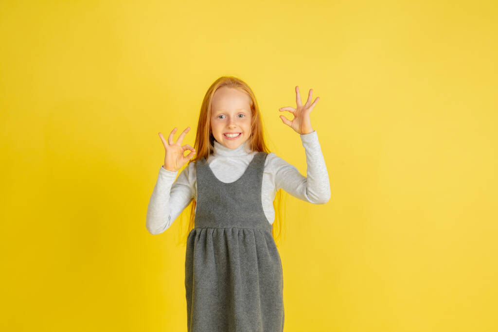 Retrato de niña caucásica con emociones brillantes aisladas en el fondo amarillo del estudio - Foto, Imagen